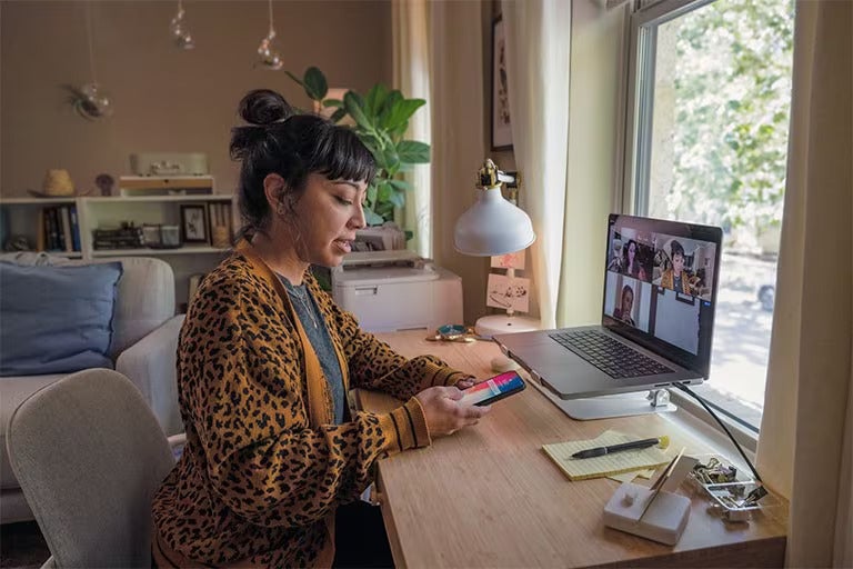 A woman sits at her desk looking at her smartphone.